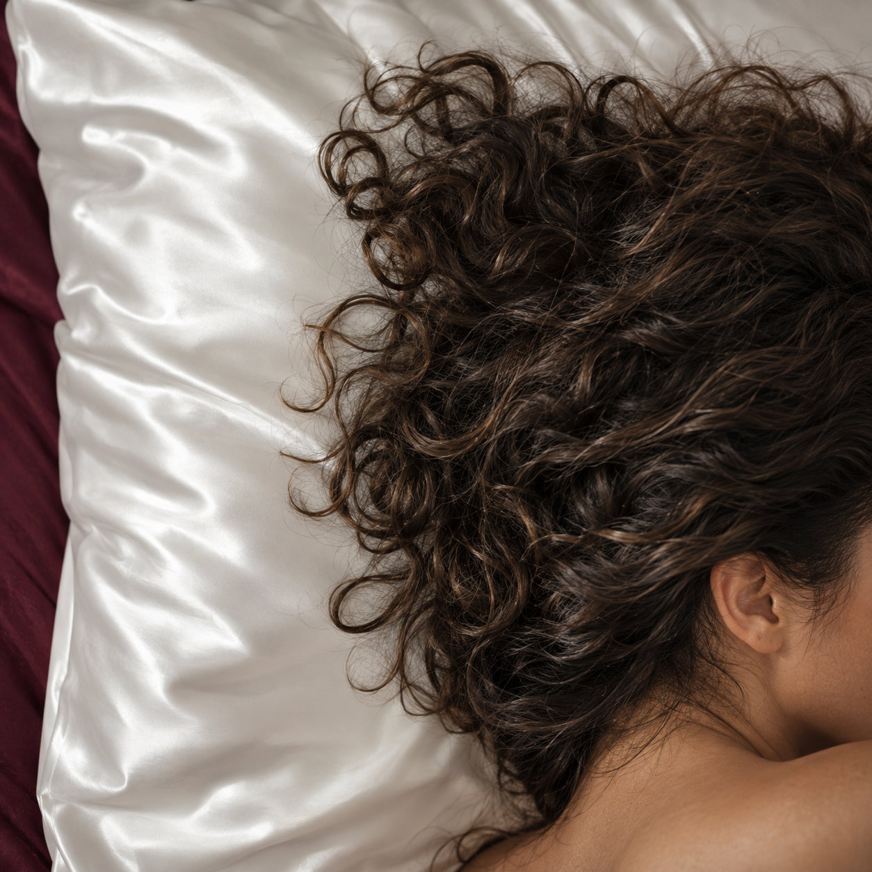 Des cheveux bouclés reposent sur une taie blanche en soie